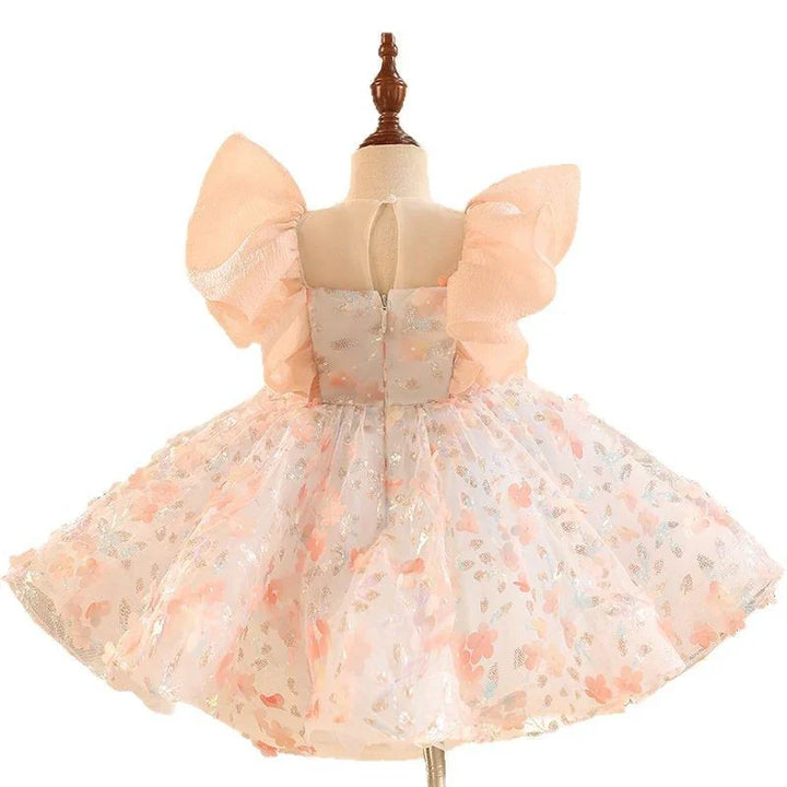 Back view of a toddler's pastel peach floral dress with puff sleeves and glitter details on a mannequin