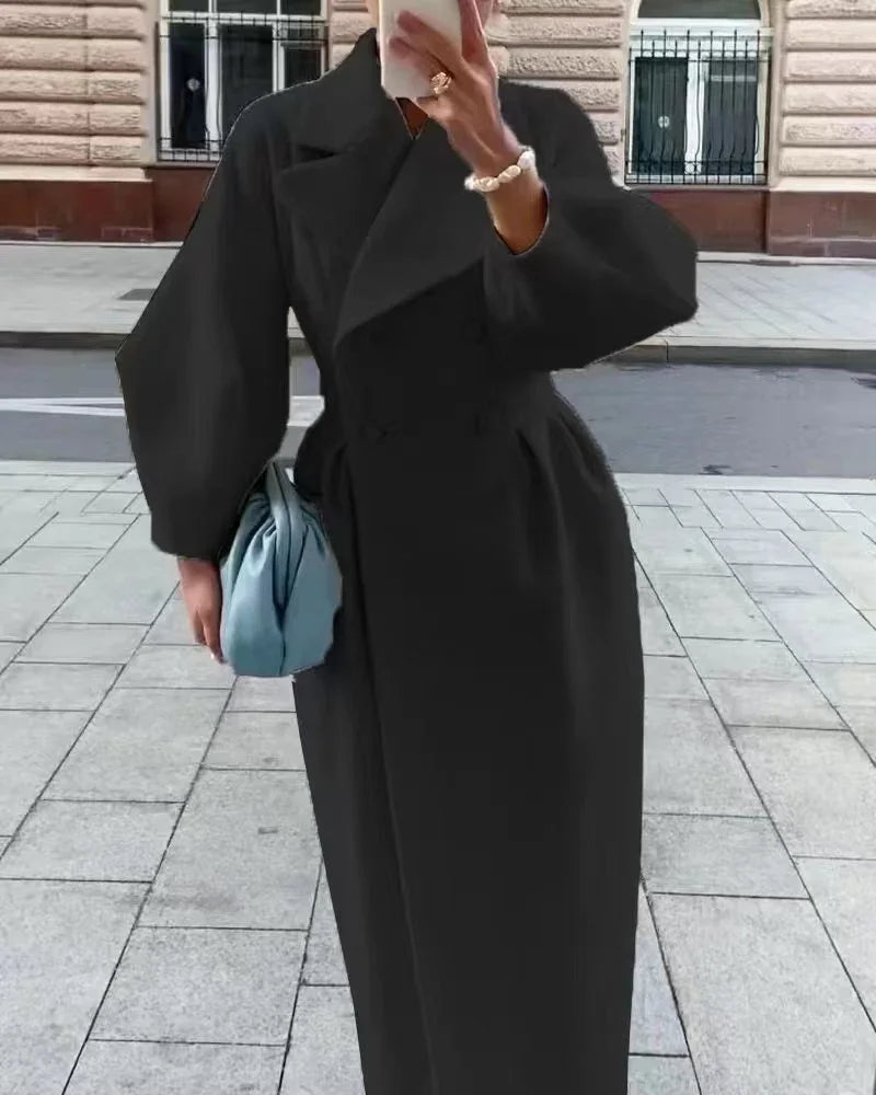 Woman in stylish black long coat holding light blue clutch bag on urban sidewalk