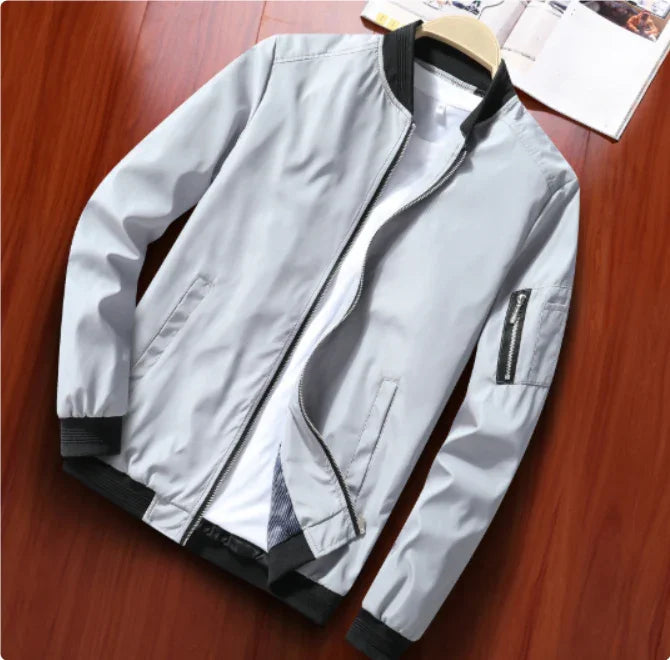 Light gray men's bomber jacket with black cuffs and collar, zippered pocket on sleeve, displayed on wooden surface