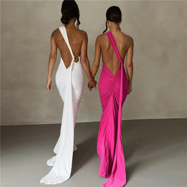 Two women holding hands wearing elegant backless ruched evening gowns in white and pink with long draped fabric trails