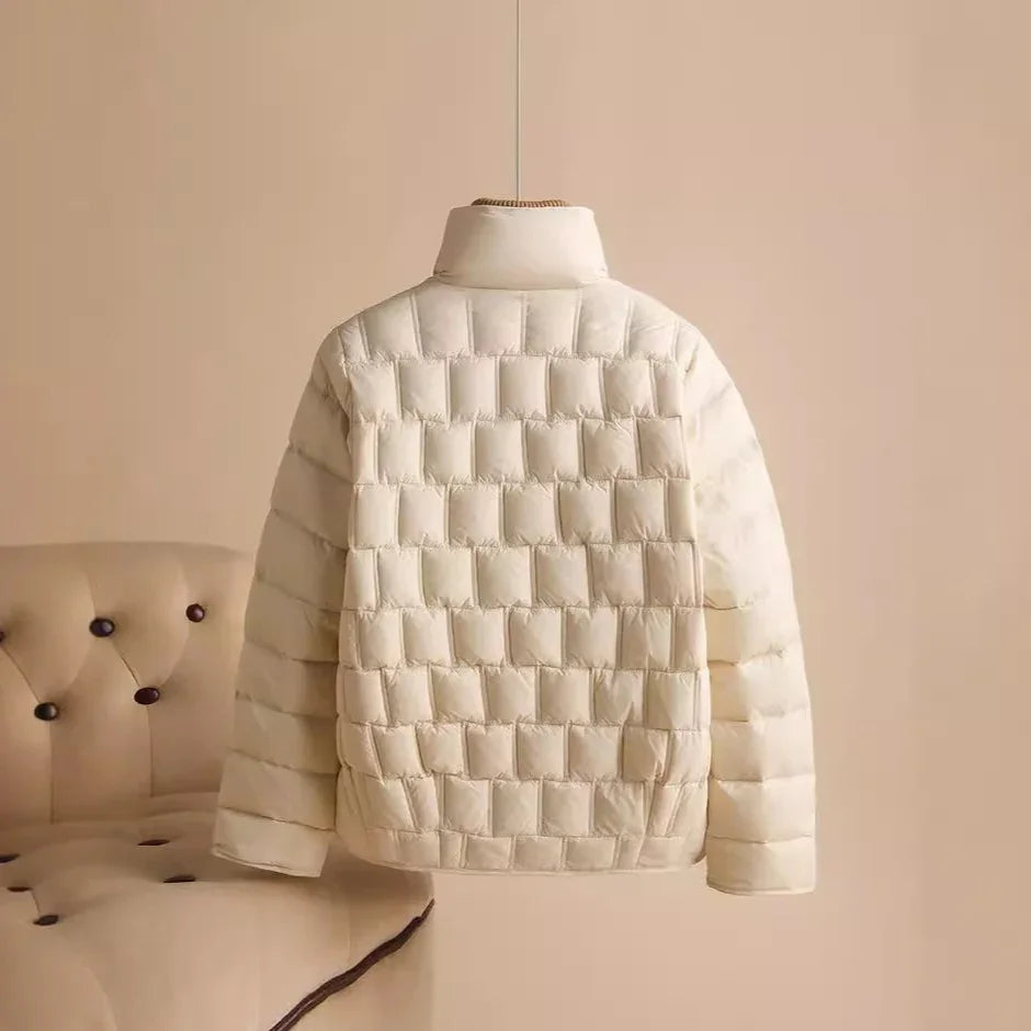 Cream-colored quilted puffer jacket hanging in minimalist beige room with tufted chair