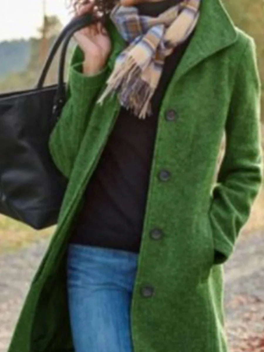 Woman wearing green coat, plaid scarf, blue jeans, carrying black handbag outdoors