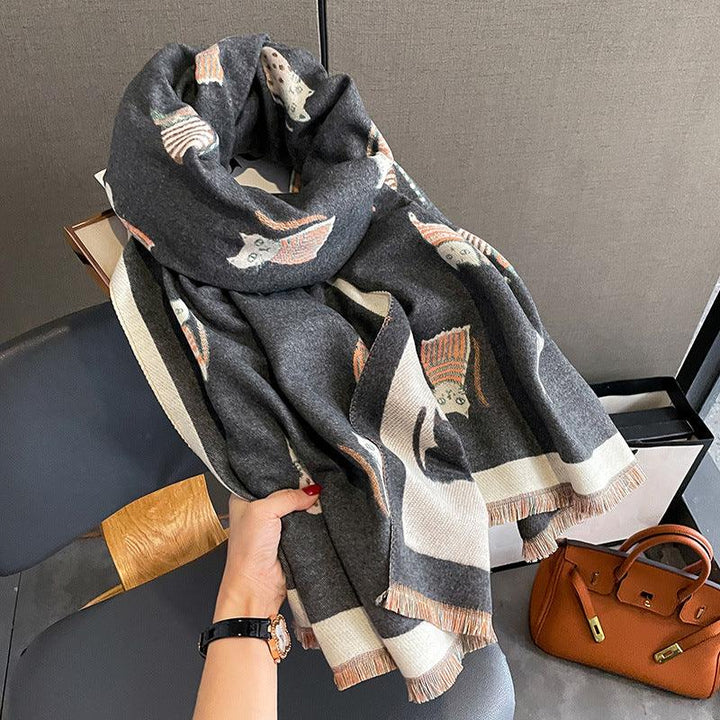 Hand holding a dark gray scarf with owl patterns and beige fringes, brown leather handbag nearby