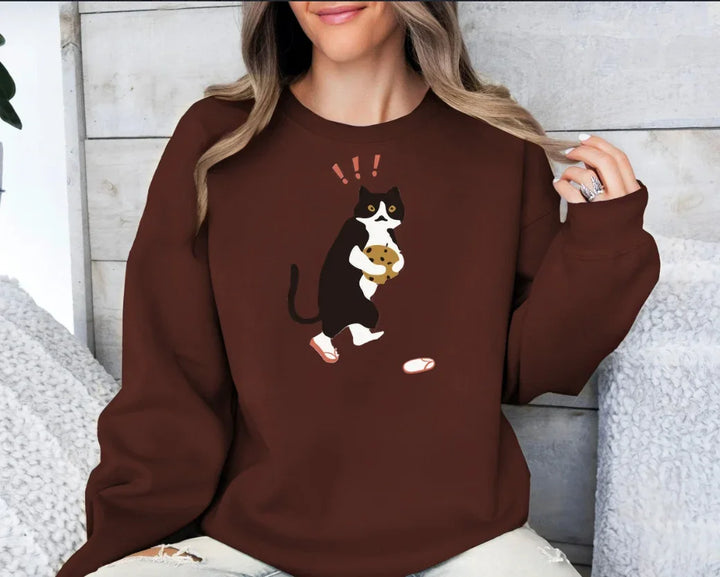 Woman wearing brown sweatshirt with graphic of black and white cat holding cookie and exclamation marks