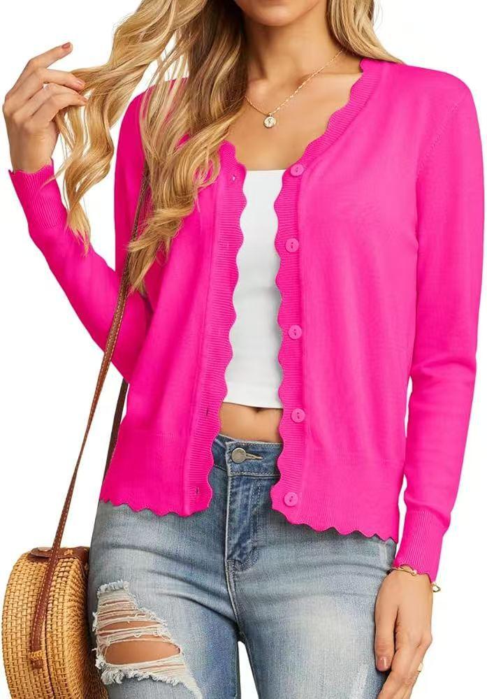 Woman wearing bright pink scalloped edge button-up cardigan with ripped jeans and woven handbag
