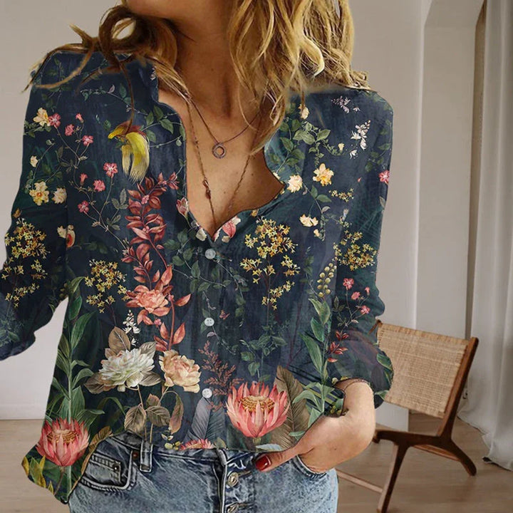 Woman wearing dark floral print blouse with long sleeves and light blue jeans indoors