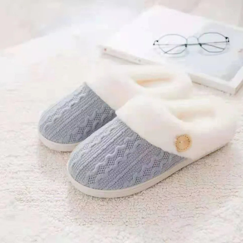Gray knit cozy slippers with white faux fur lining on plush carpet near glasses and book