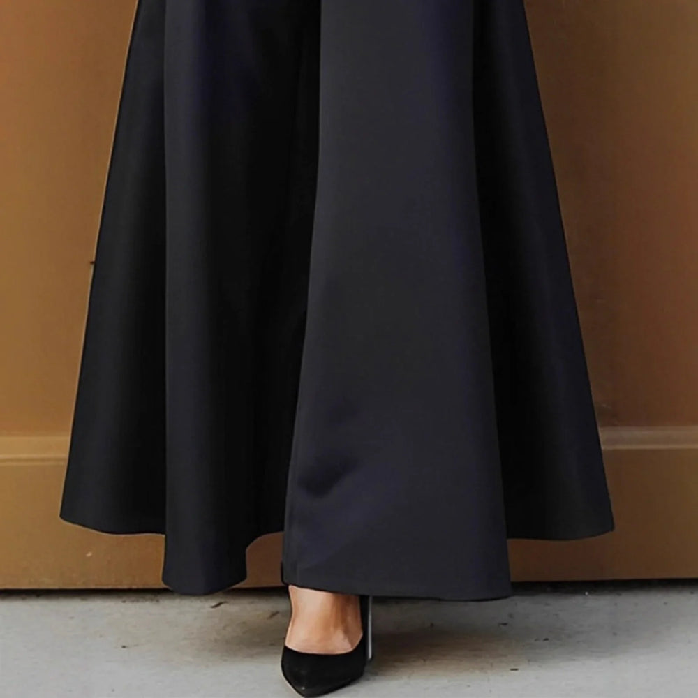 Black wide-leg pants with black pointed-toe heels on concrete floor and brown background