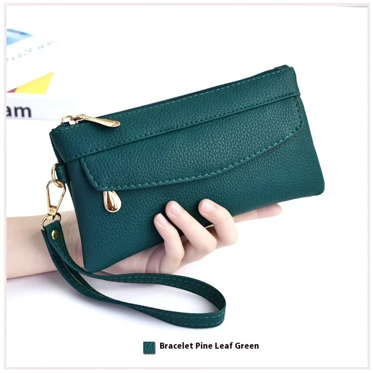 Hand holding a pine leaf green textured leather wristlet wallet with gold zipper and strap