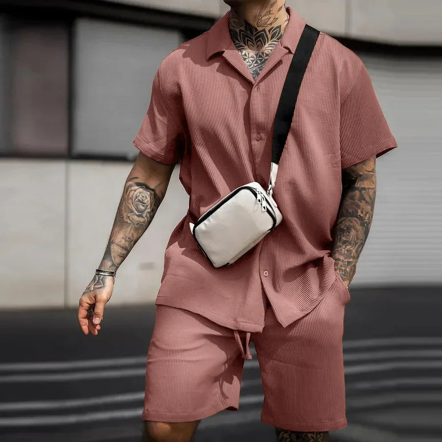 Man wearing pink ribbed short-sleeve shirt and matching shorts with white crossbody bag and tattoos