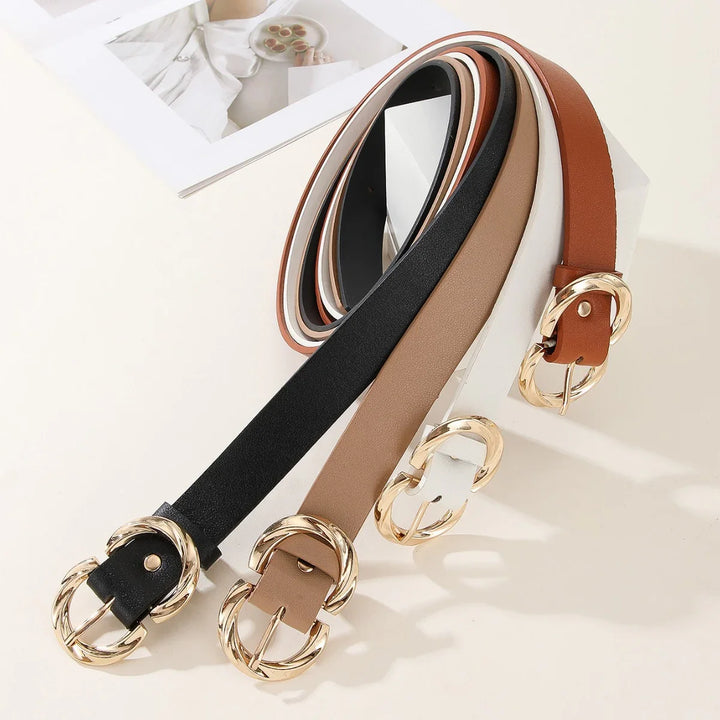 Set of stylish black, beige, white, and brown leather belts with gold oval buckles on white surface