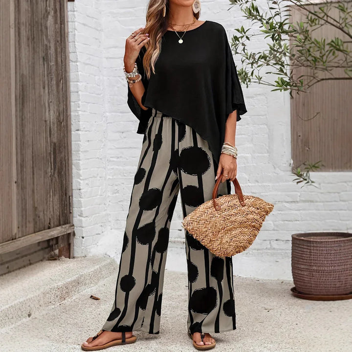 Woman in black asymmetrical top and wide-leg pants with black circle print holding woven handbag outdoors
