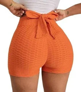 Woman wearing high waisted textured orange shorts with a bow tie back