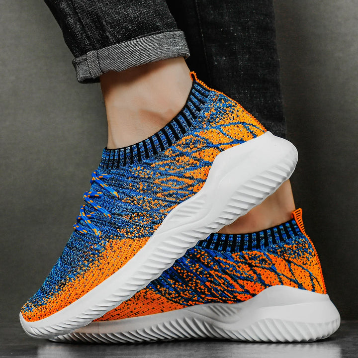 Close-up of orange and blue knit sneakers with white sole, worn with rolled-up black jeans