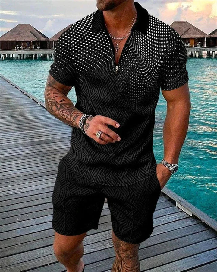Muscular man wearing black patterned short-sleeve shirt and shorts, standing on wooden pier by turquoise water and overwater bungalows