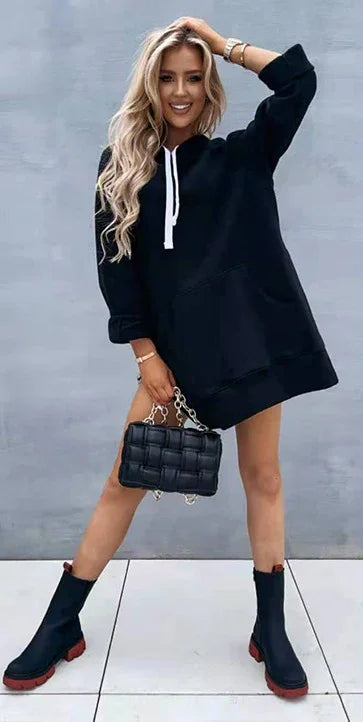 blonde woman wearing black oversized hoodie dress and black ankle boots holding black quilted handbag