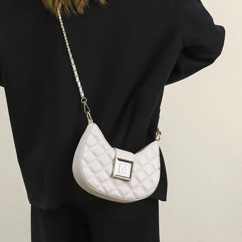 White quilted leather crossbody bag with gold hardware and chain strap worn with black outfit