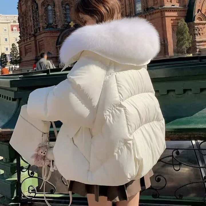 Woman wearing white puffer jacket with large fur collar holding white handbag with teddy bear charm outdoors