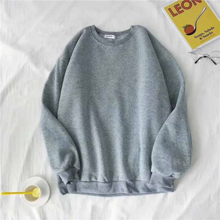 Grey crewneck sweatshirt laid flat on white fabric with clear glasses and yellow cookbook