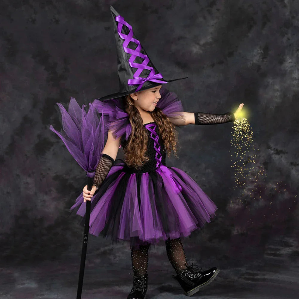 Little girl in purple and black witch costume with pointey hat and glowing magic dust on dark background