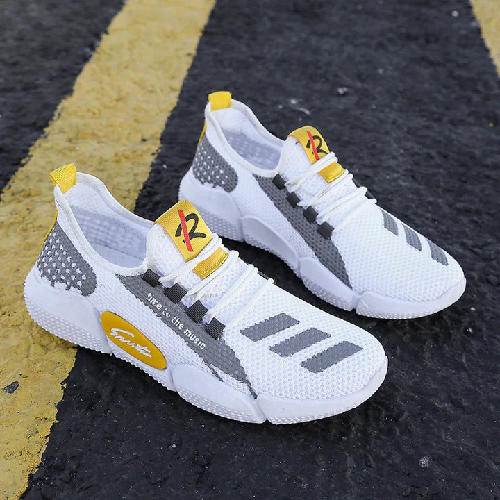 White and gray breathable knit sneakers with yellow accents on a black asphalt road