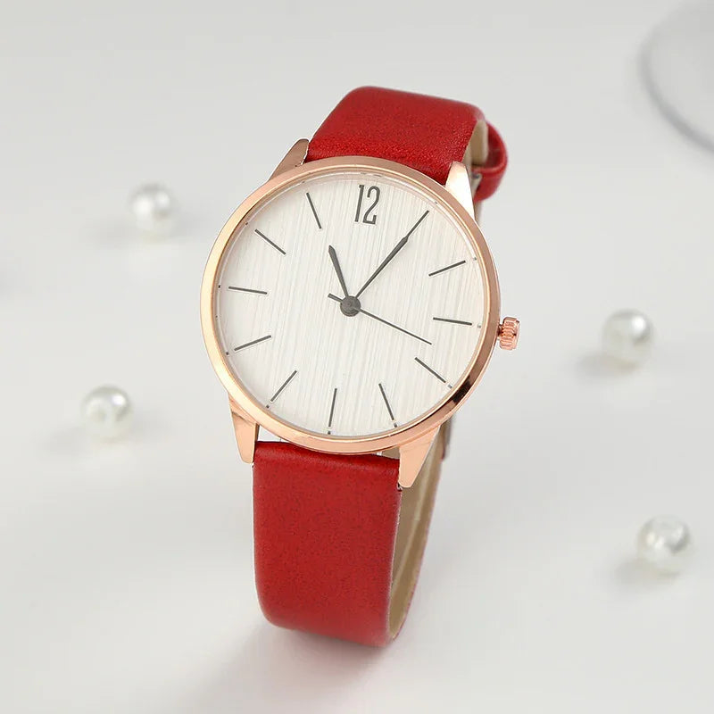 Minimalist wristwatch with rose gold case, white textured dial, and red leather strap on light background