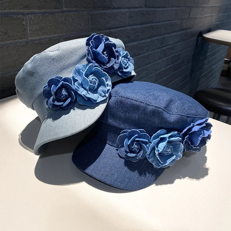 Two denim caps with decorative blue fabric flower accents displayed on a white surface with a brick wall background