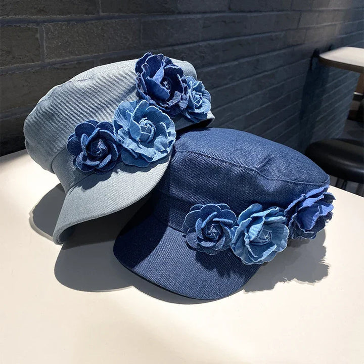Two denim caps with decorative blue fabric flower accents displayed on a white surface with a brick wall background
