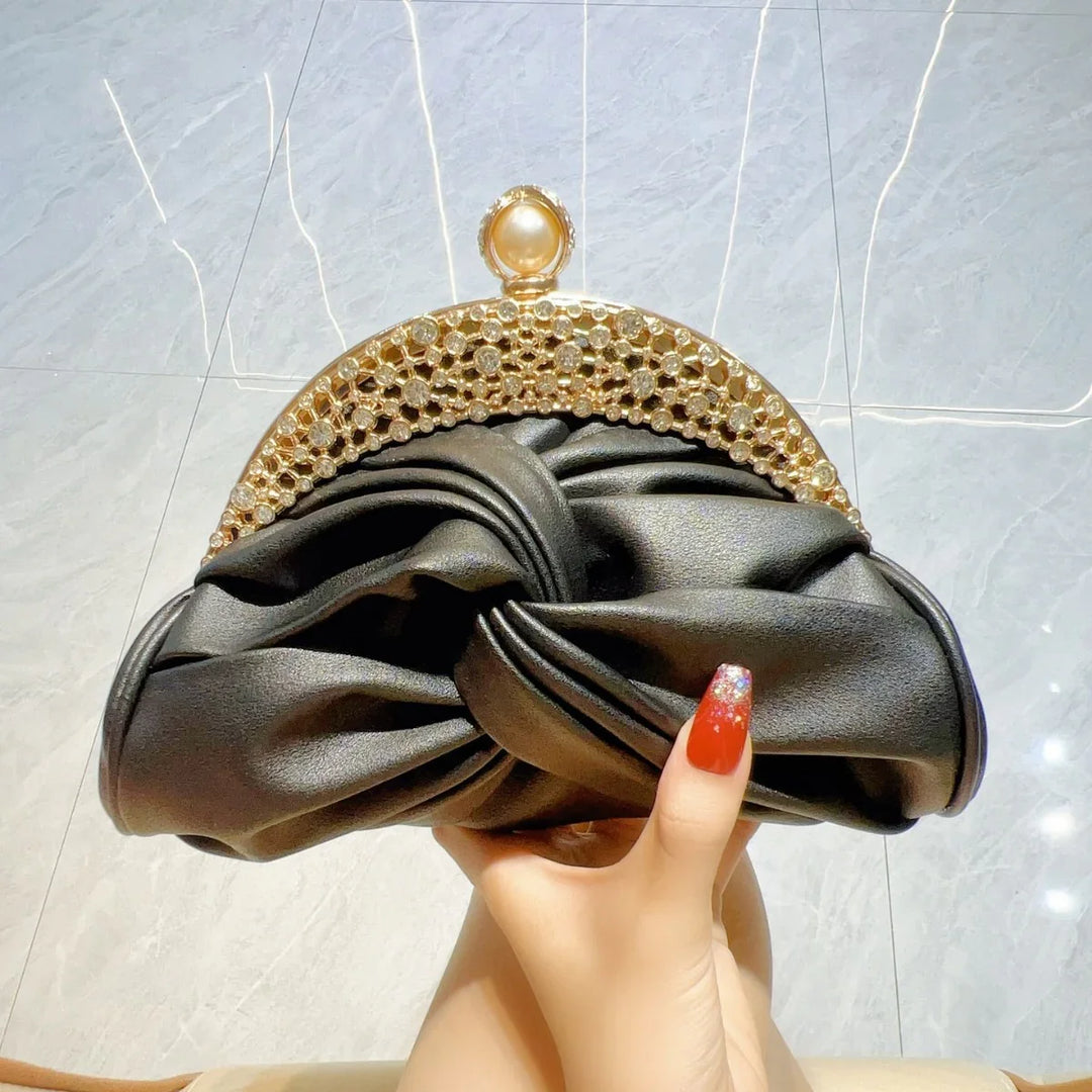 Black ruched satin clutch purse with gold jeweled frame and pearl clasp held by hand with red glitter nails