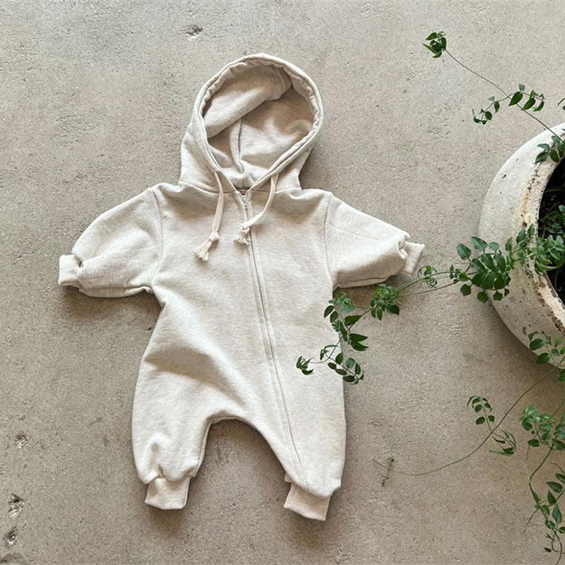 Beige zip-up baby hoodie jumpsuit with hood and rolled sleeves on concrete floor next to green potted plant