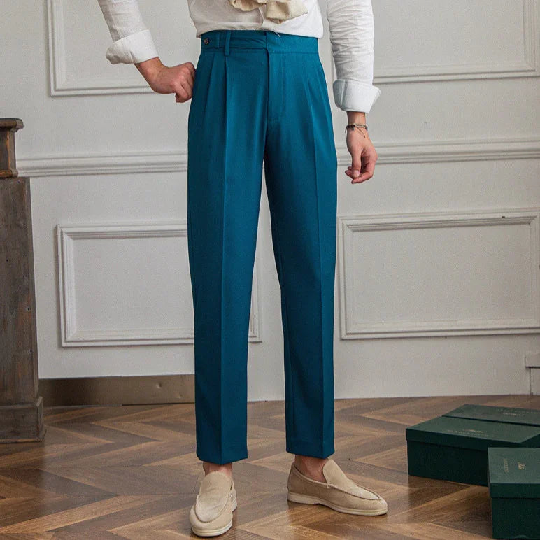 Person wearing teal tailored pants with front pleats and beige loafers in a room with wooden floor