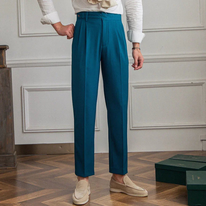 Person wearing teal tailored pants with front pleats and beige loafers in a room with wooden floor