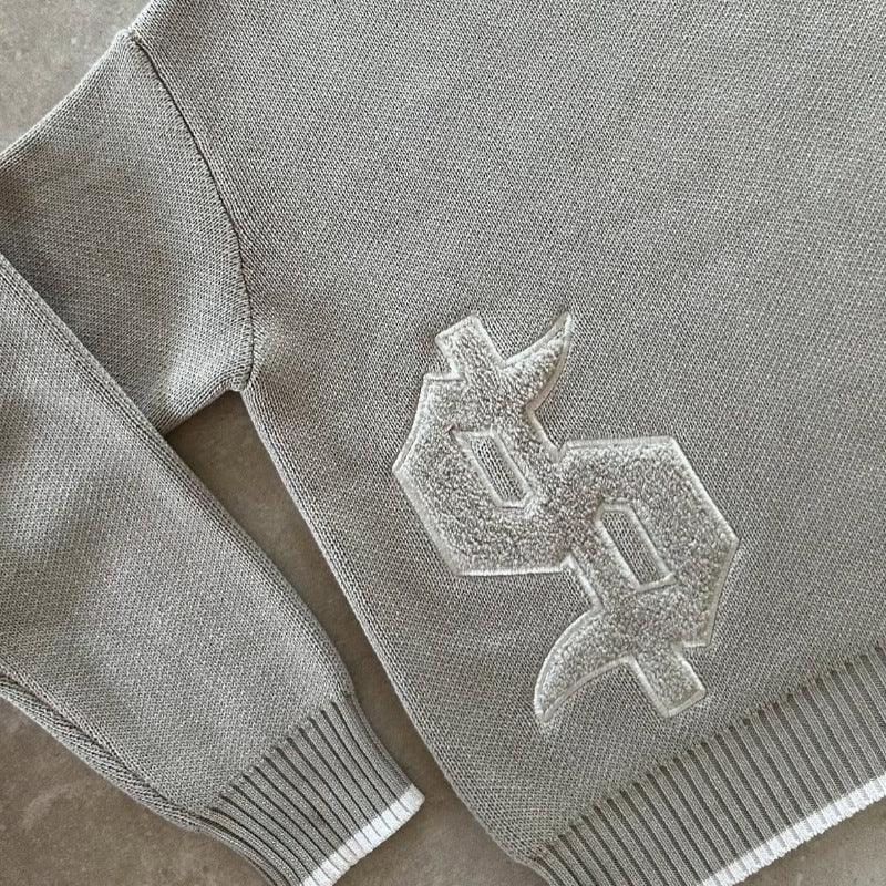 Close-up of gray knitted sweater with white textured embroidered initials 'SP' on front