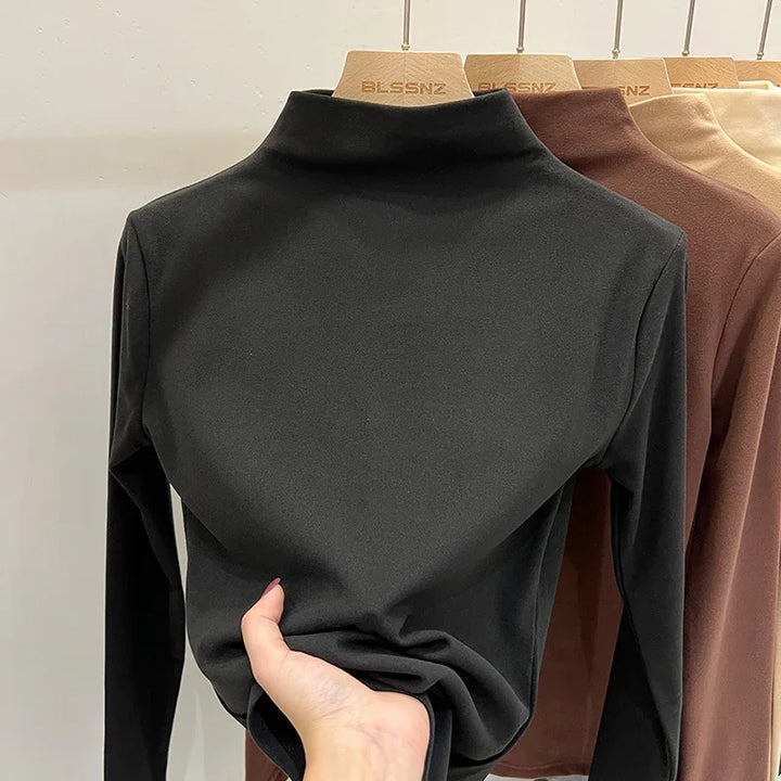 Black long sleeve turtleneck top on wooden hanger with brown and beige tops in background