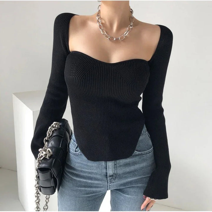 Woman wearing black ribbed off-shoulder sweater with silver chain necklace and holding black chain strap bag