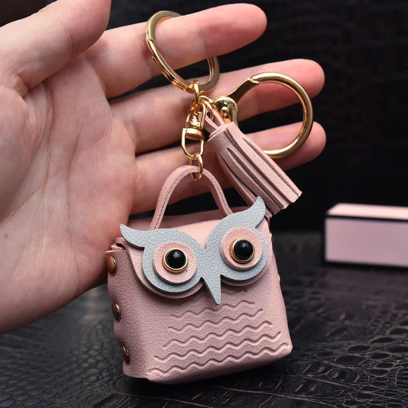 hand holding pink owl-shaped mini purse keychain with tassel and gold ring on black surface