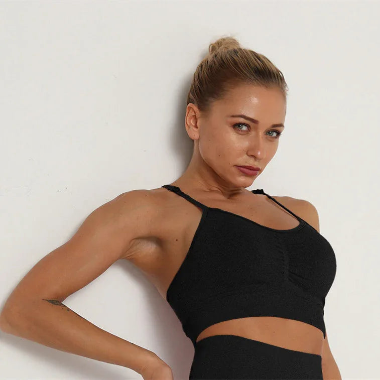 Fit woman with blonde hair in a black workout crop top posing against white wall