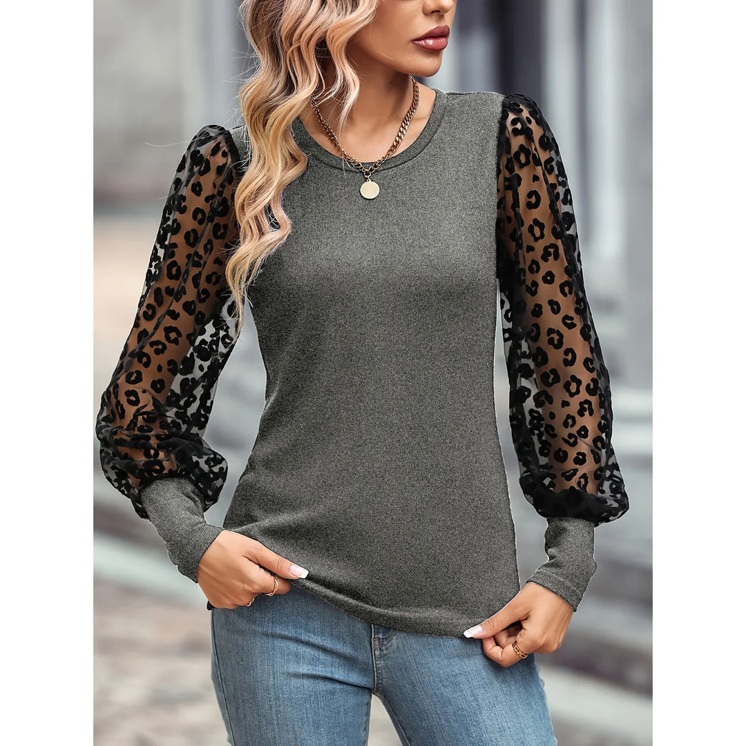Woman wearing gray top with sheer black leopard print puff sleeves and blue jeans