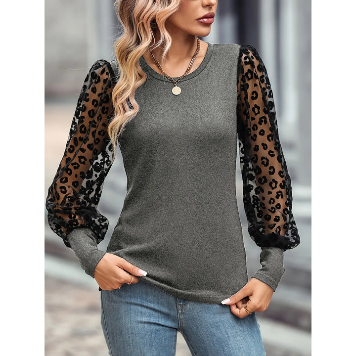 Woman wearing gray top with sheer black leopard print puff sleeves and blue jeans