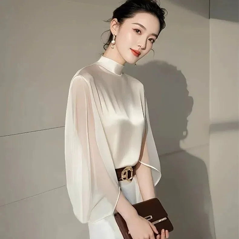 Elegant woman in a white satin blouse with flowing sleeves, holding a brown clutch bag indoors