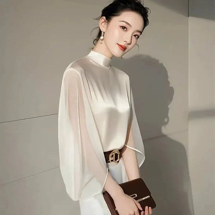 Elegant woman in a white satin blouse with flowing sleeves, holding a brown clutch bag indoors