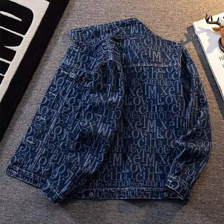 Blue denim jacket with all-over abstract letters pattern laid on gray carpet near black and white rug