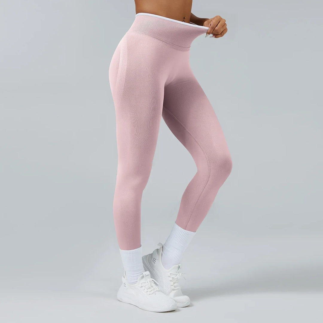 Woman wearing high-waisted pink seamless leggings with white socks and sneakers on gray background