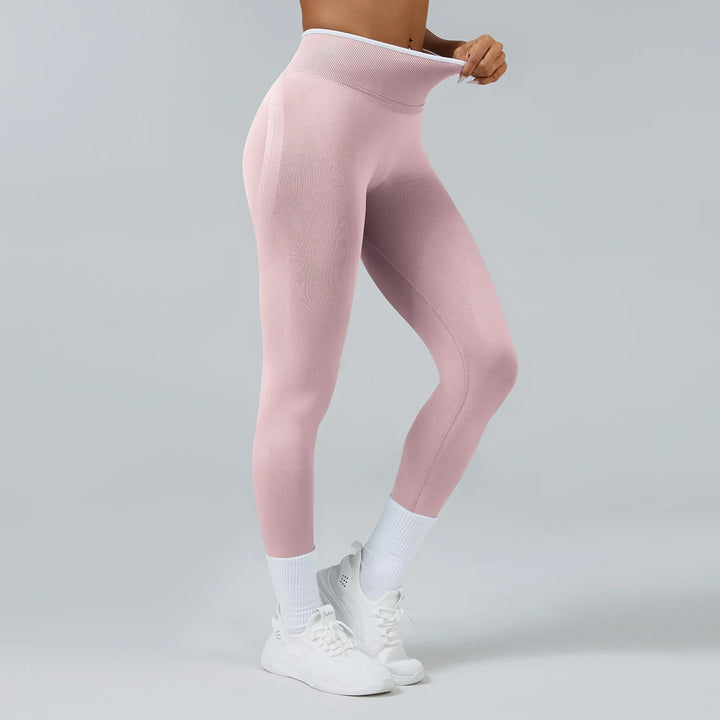 Woman wearing high-waisted pink seamless leggings with white socks and sneakers on gray background