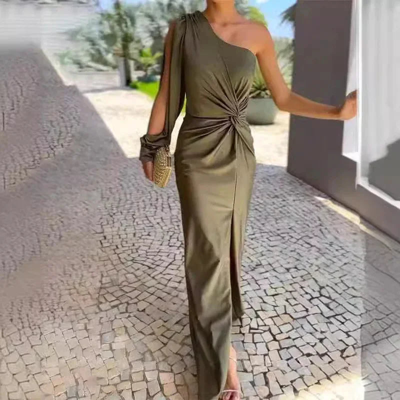 Woman wearing olive green one-shoulder maxi dress with front slit and ruched waist, holding woven clutch