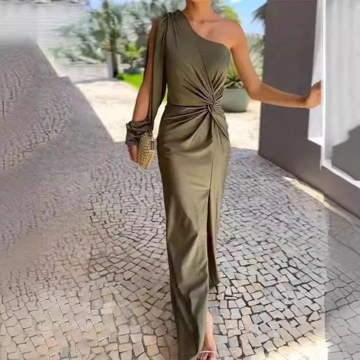 Woman wearing olive green one-shoulder maxi dress with front slit and ruched waist, holding woven clutch