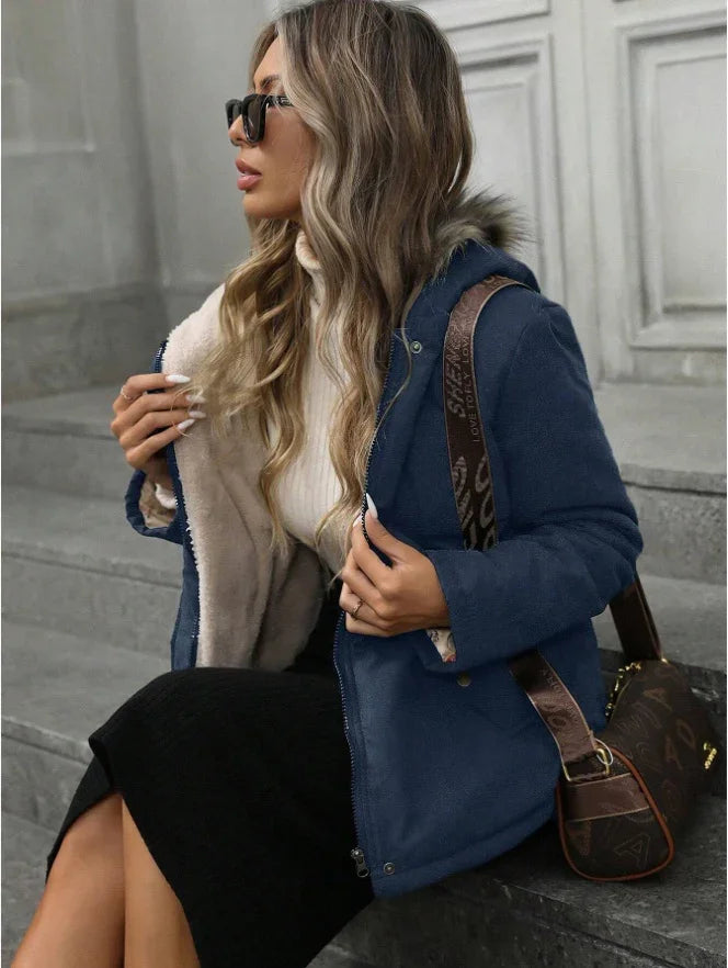 Woman wearing blue fur-lined jacket, black skirt, white turtleneck, sunglasses, and brown designer handbag sitting on stone steps