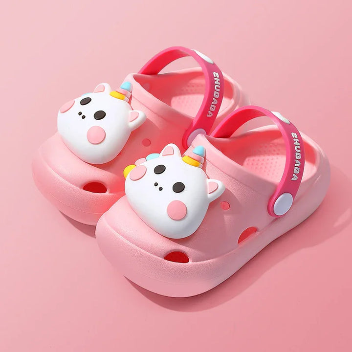 Pink kids clogs with unicorn face charms and adjustable heel straps on pink background