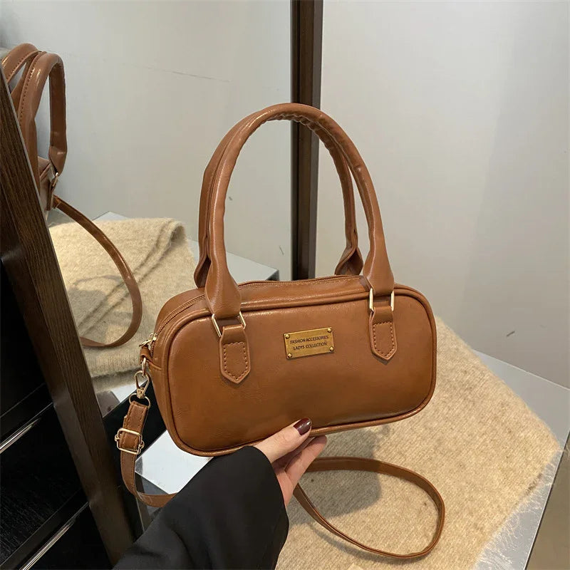 Brown leather handbag with two handles and shoulder strap displayed near a mirror and beige fabric