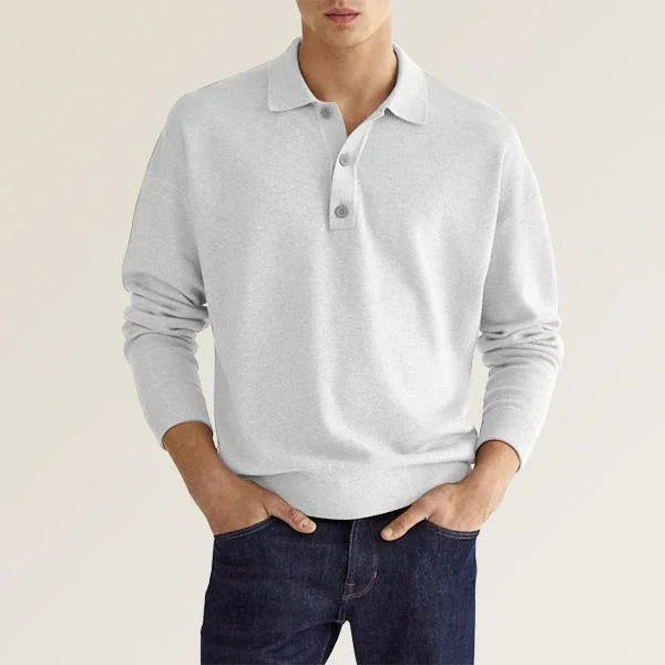 Man wearing light gray long sleeve polo shirt paired with dark blue jeans against neutral background